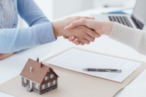Handshake over a property contract with a house model on the table, symbolizing financing agreements in the real estate market.